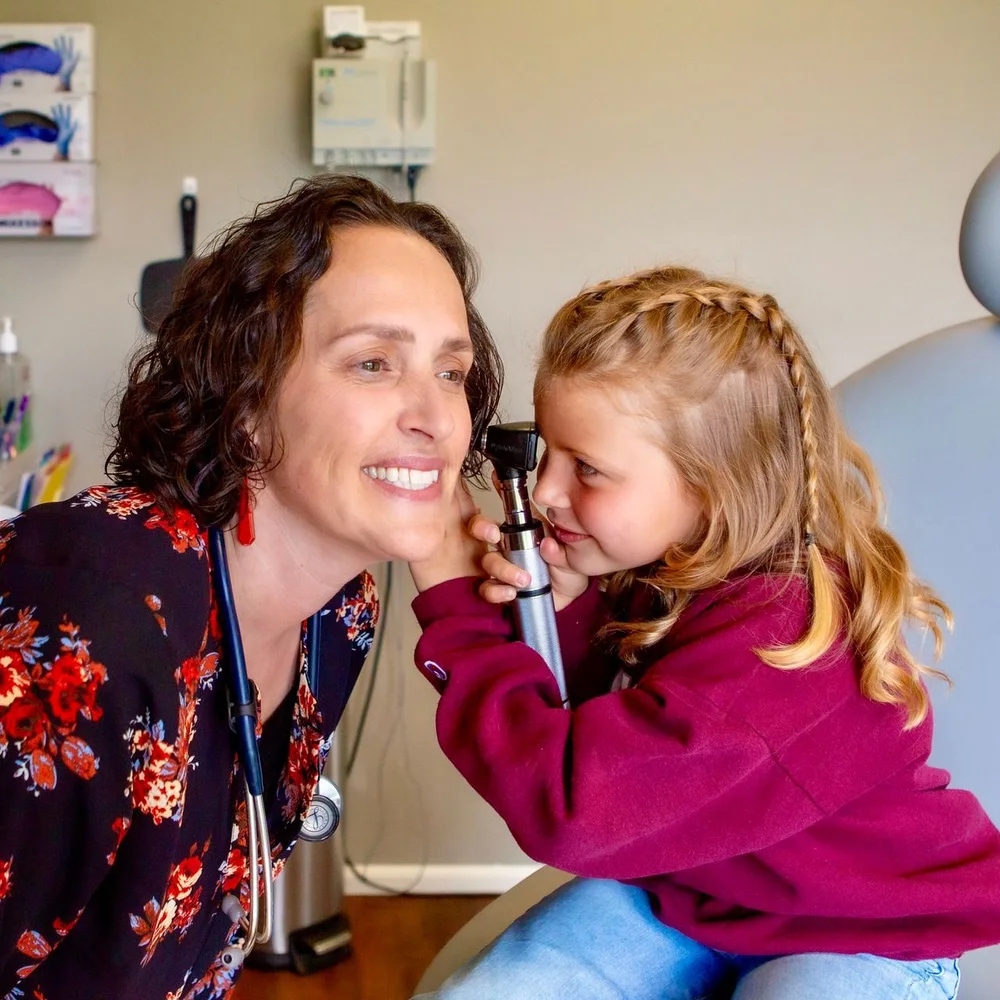 A CoreMed clinician letting a young patient hold the otoscope during a visit