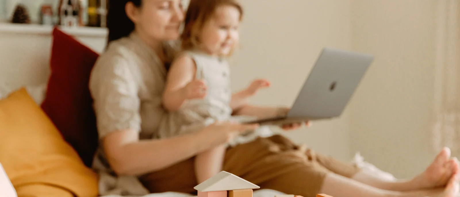A parent and toddler on a bed with a laptop open for a video visit